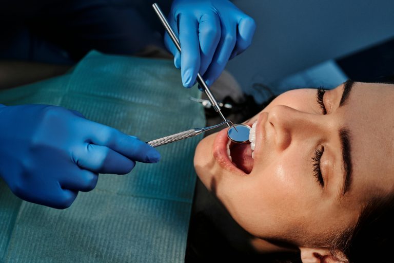 A patient in a dental chair receives care from a dentist wearing blue gloves and using dental instruments.